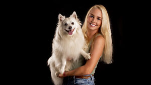 Young woman holds white dog on black background